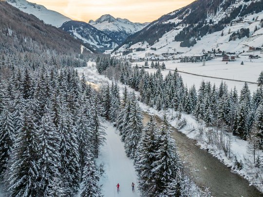 Jesacherhof: Ihr Hotel im Defereggental Zwei Langläufer auf verschneiter Strecke zwischen Tannen im Tal bei Sonnenuntergang