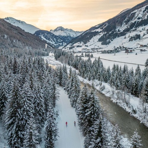 Excursions to the St. Jakob in Defereggental ski resort Two cross-country skiers on snowy trail through trees in valley at sunset