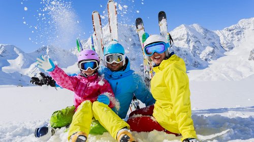 Tobogganing in Tyrol – fun for the whole family Family in colorful ski gear playing in the snow with snowy mountains in background