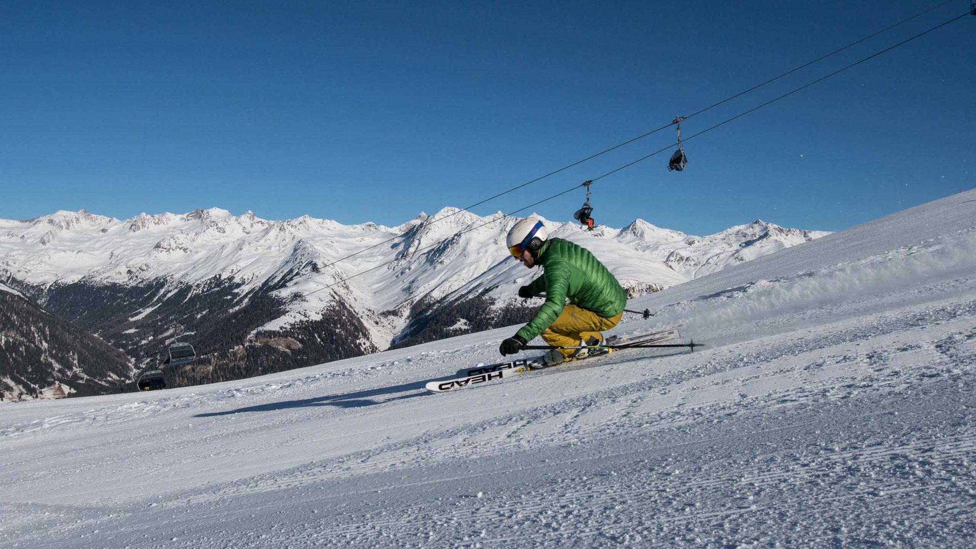 Excursions to the St. Jakob in Defereggental ski resort Skier in green jacket and yellow pants turning on snow-covered slope