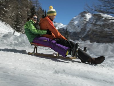 Tobogganing in Tyrol – fun for the whole family Two people sledding together on snow with mountains in the background