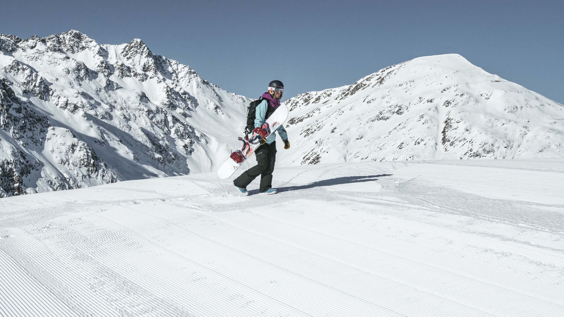 Excursions to the St. Jakob in Defereggental ski resort Snowboarder walking on groomed slope with snowy mountains in background
