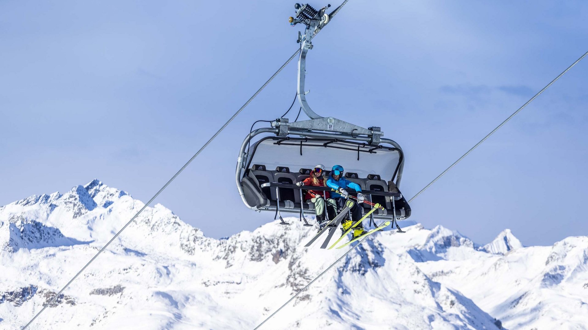 Excursions to the St. Jakob in Defereggental ski resort Two skiers on a chairlift over snow-covered mountains