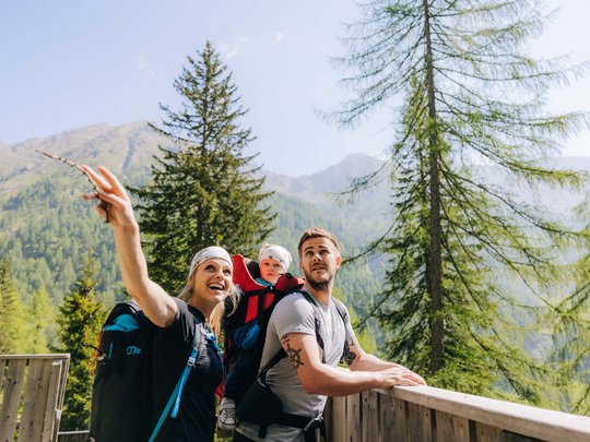 Jesacherhof: Ihr Hotel im Defereggental Familie mit Baby auf Bergwanderung in Landschaft mit Tannenbäumen und Bergen